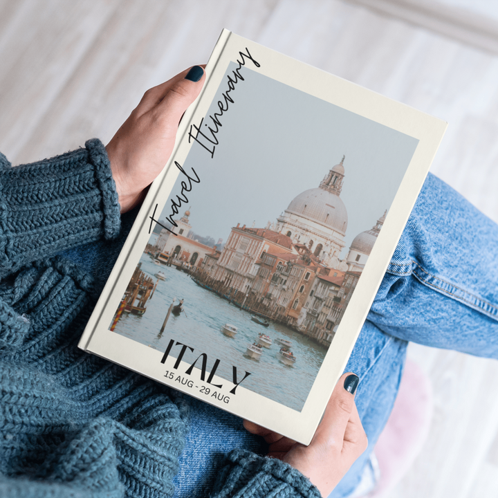 Person holding a travel itinerary book with a photo of Venice, Italy on the cover.