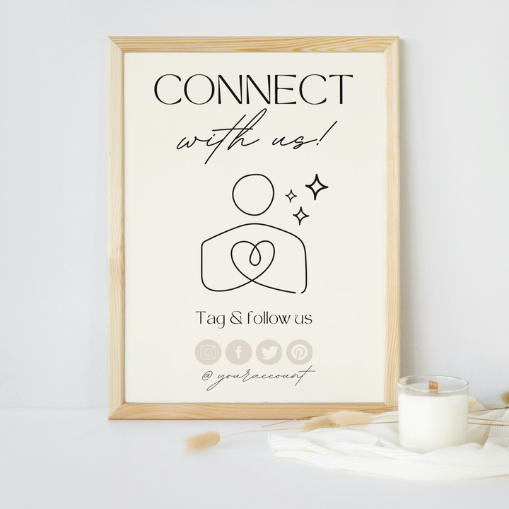 Framed sign with the text 'Connect with us! Tag & follow us' and social media icons, displayed on a white surface next to a lit candle.