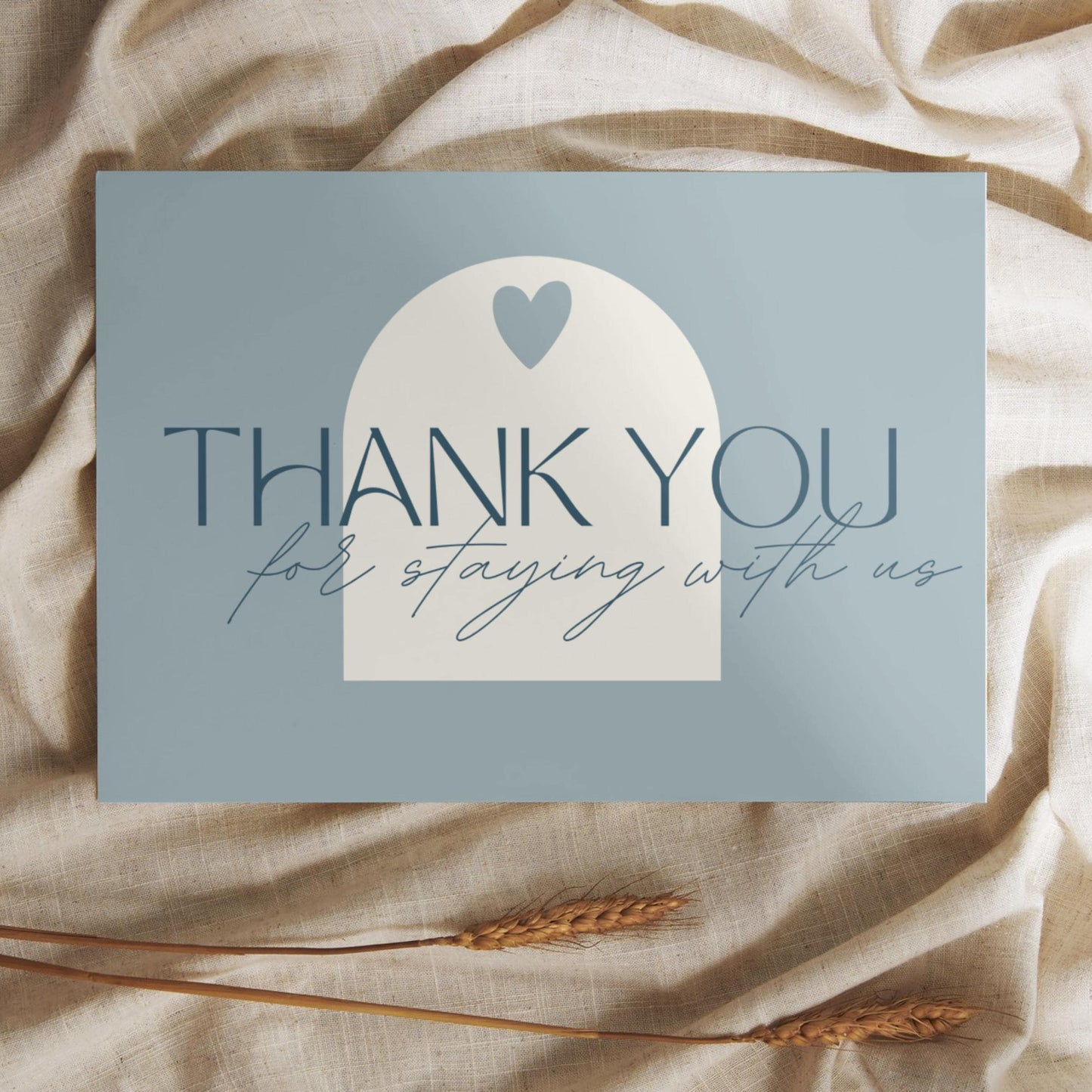 Thank you card with the message 'Thank you for staying with us' in elegant typography, placed on a soft beige fabric with wheat stalks.