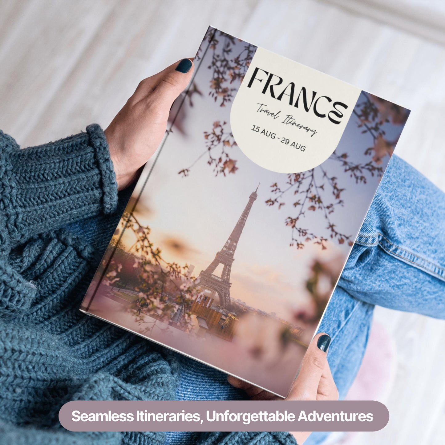 A person wearing a cozy blue sweater and jeans is holding a hardcover travel itinerary book.
