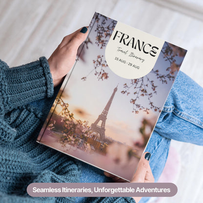 A person wearing a cozy blue sweater and jeans is holding a hardcover travel itinerary book.