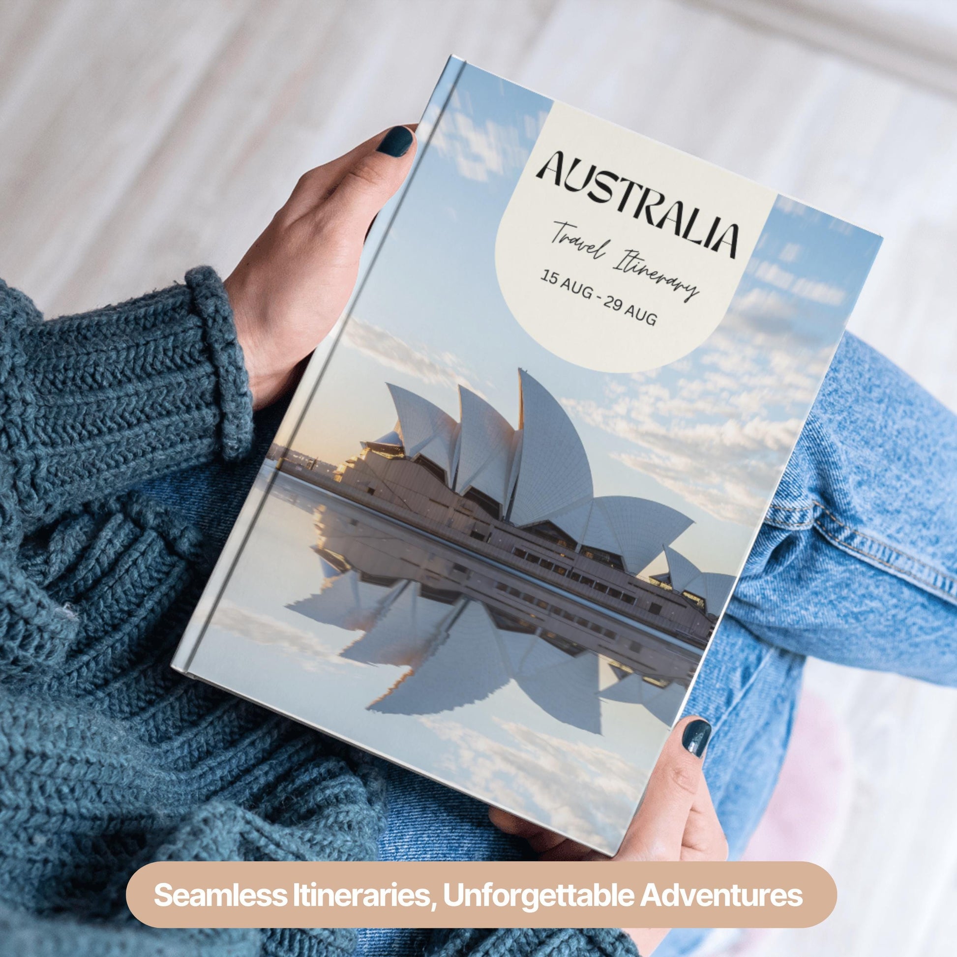 A person wearing a cozy blue sweater and jeans is holding a hardcover travel itinerary book.