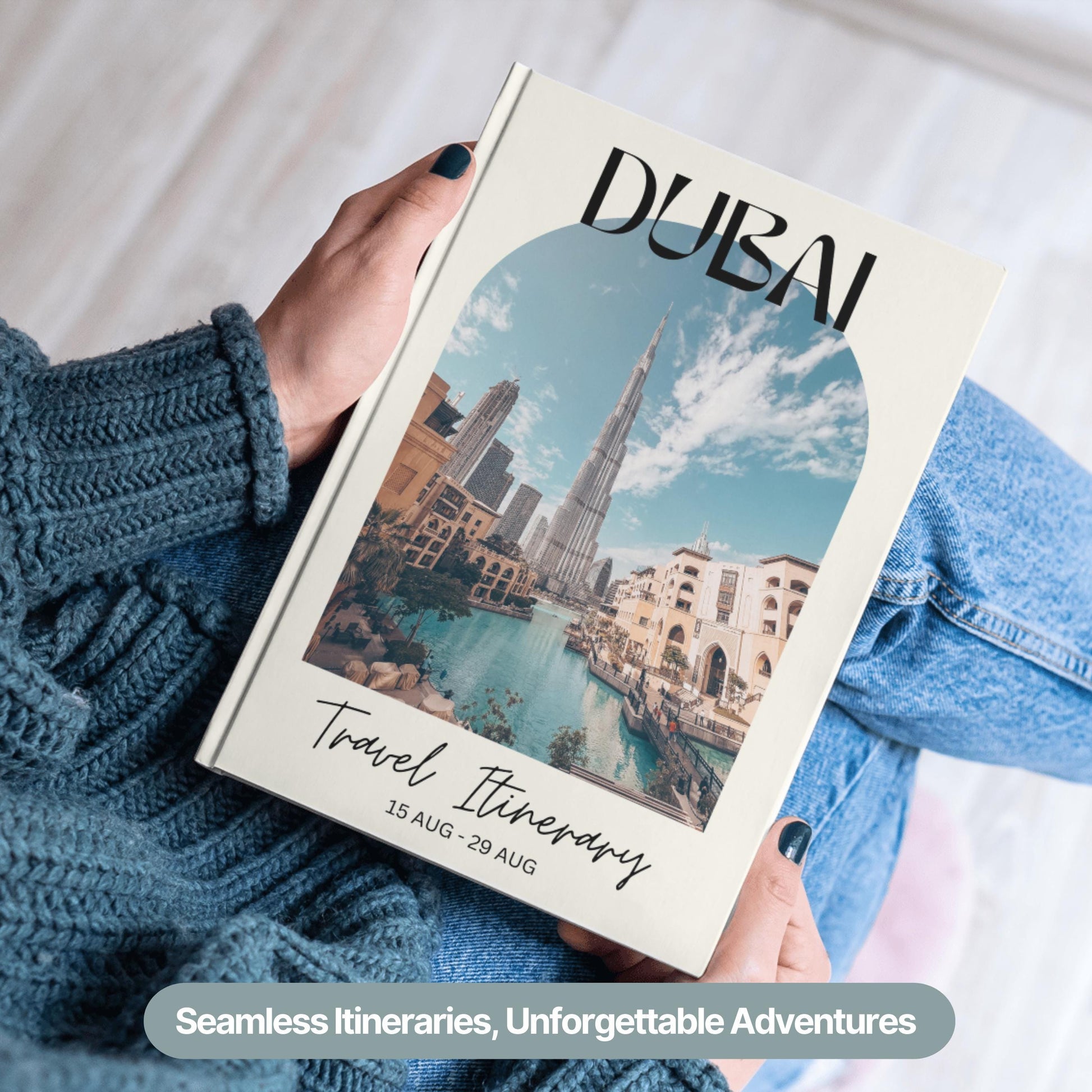 A person wearing a cozy blue sweater and jeans is holding a hardcover travel itinerary book.