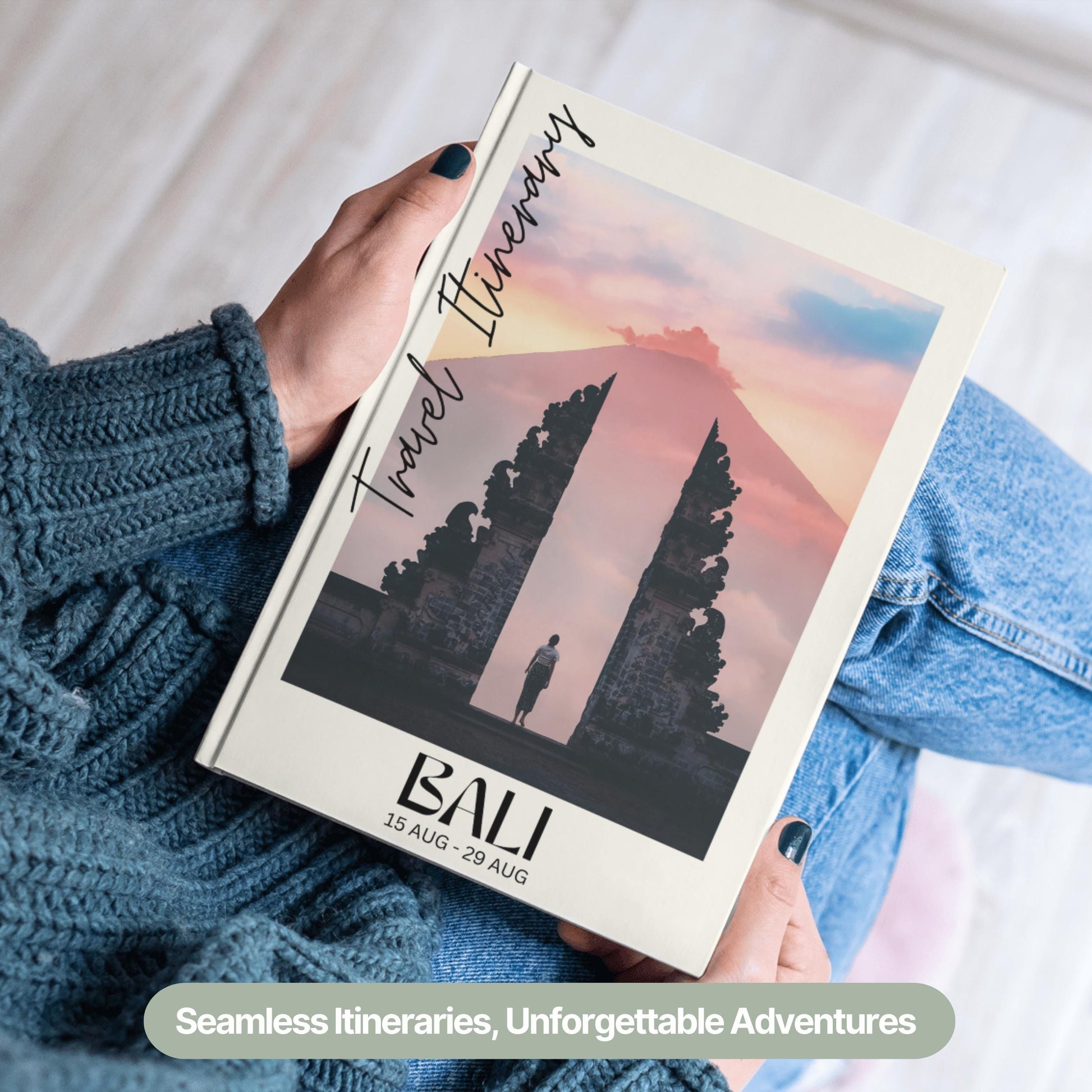A person wearing a cozy blue sweater and jeans is holding a hardcover travel itinerary book.