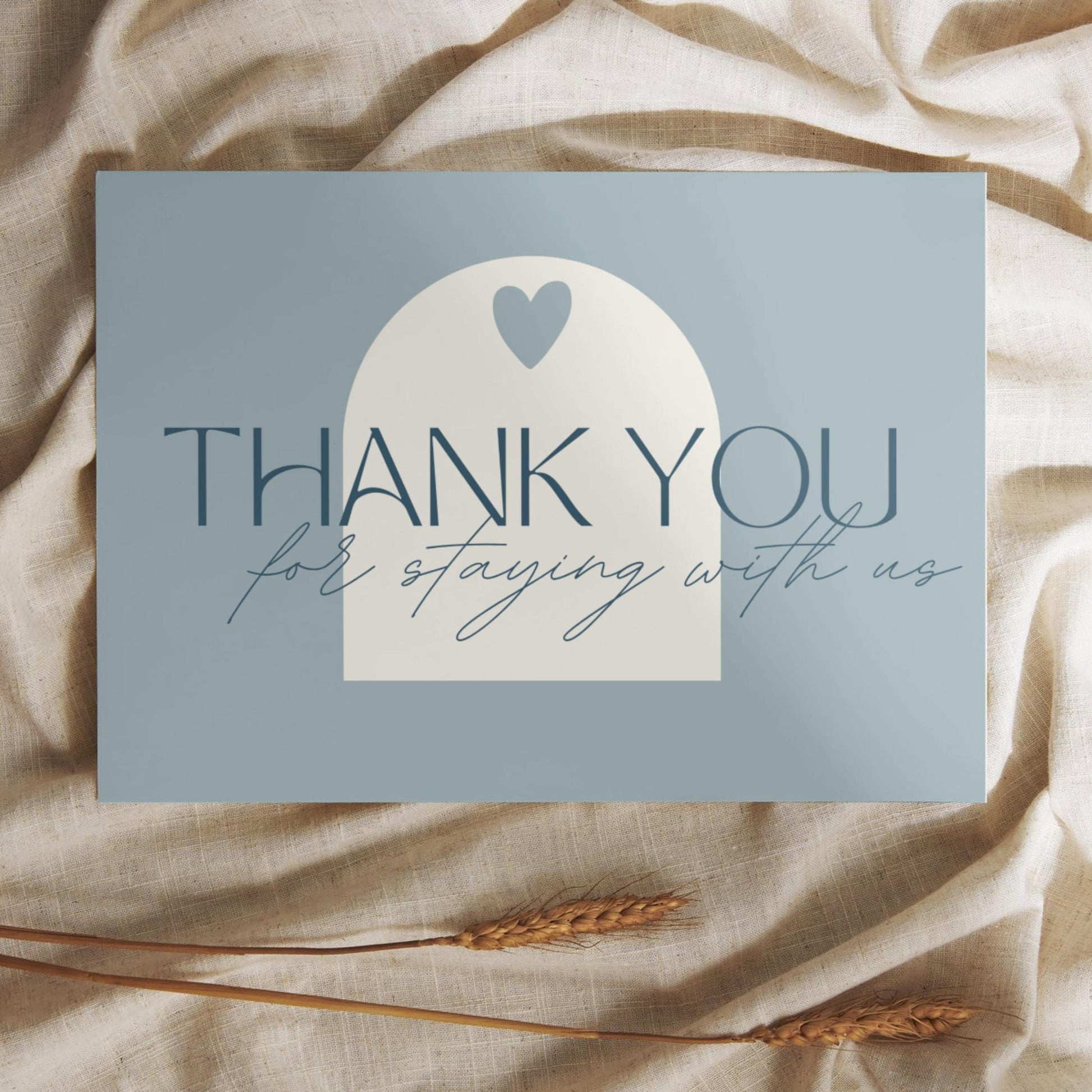Thank you card with the message 'Thank you for staying with us' in elegant typography, placed on a soft beige fabric with wheat stalks.