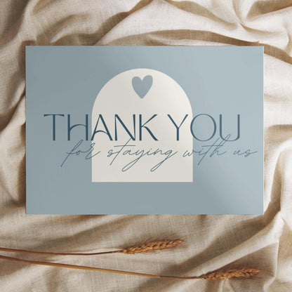 Thank you card with the message 'Thank you for staying with us' in elegant typography, placed on a soft beige fabric with wheat stalks.