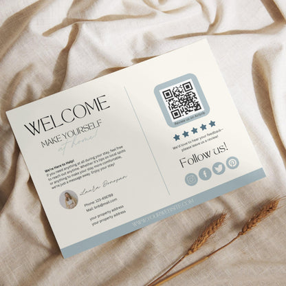Flat lay of a modern Airbnb welcome card featuring guest information, a QR code for reviews, and social media icons, placed on a light linen fabric with dried wheat stalks.