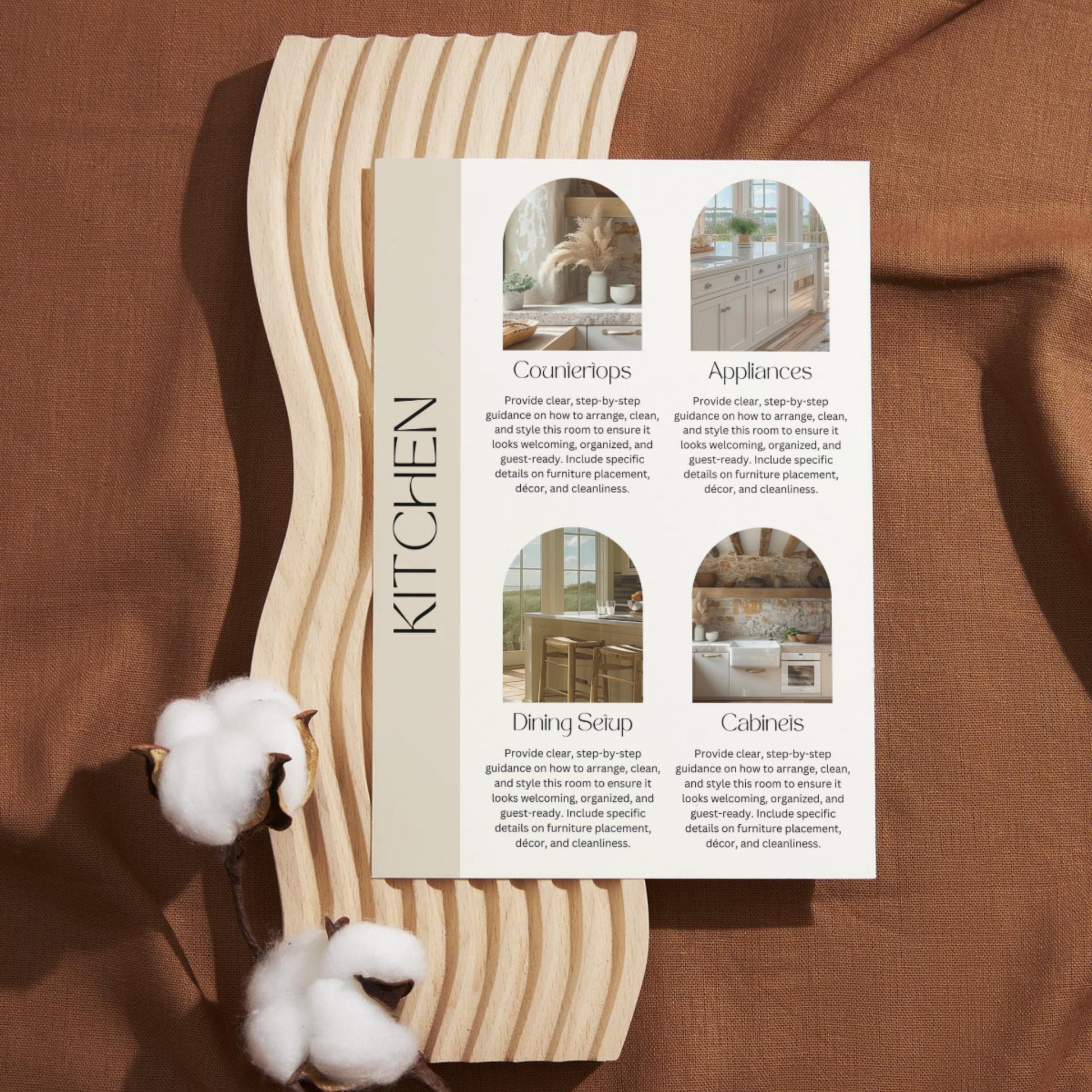A printed kitchen guide card is placed on a decorative light wood board with a wavy edge, resting on a brown fabric background. The card is titled "KITCHEN" vertically on the left and features four labeled sections with images: Countertops, Appliances, Dining Setup, and Cabinets. 