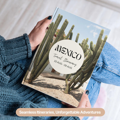 A person wearing a cozy blue sweater and jeans is holding a hardcover travel itinerary book.