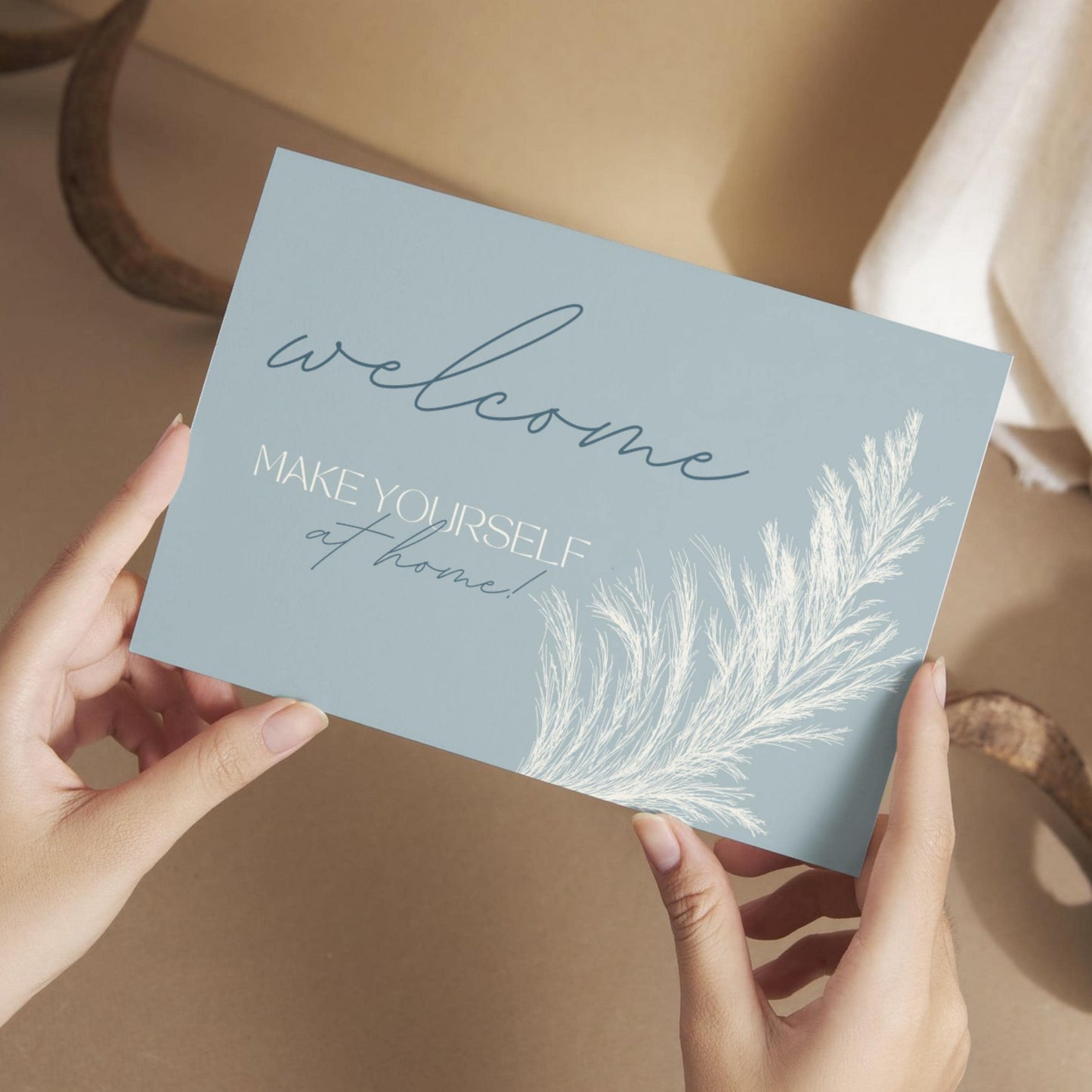 Hands holding a welcome card that reads 'Welcome, make yourself at home!' with a soft botanical illustration.