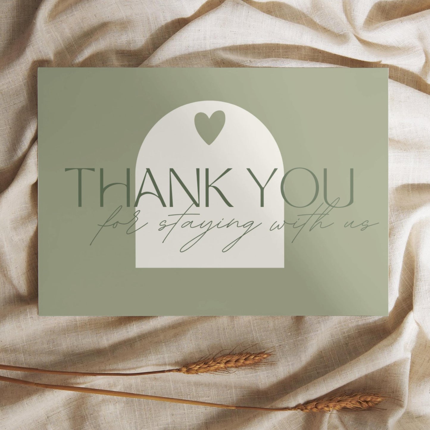 Thank you card with the message 'Thank you for staying with us' in elegant typography, placed on a soft beige fabric with wheat stalks.