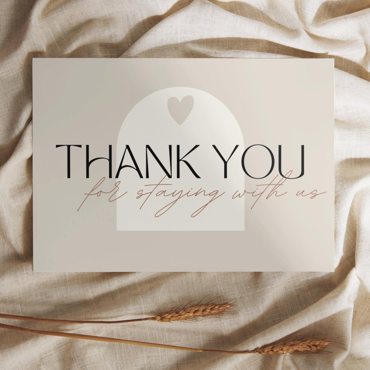 Thank you card with the message 'Thank you for staying with us' in elegant typography, placed on a soft beige fabric with wheat stalks.